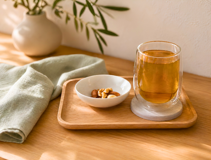 Glass of tea on a wooden tray with a bowl of nuts and a plant in the background