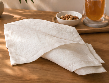 White linen napkin on a wooden table with a bowl of nuts and a glass of tea in the background.