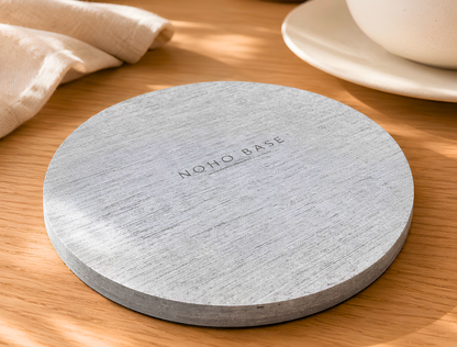 Round stone coaster with 'NOHO BASE' branding on a wooden surface.