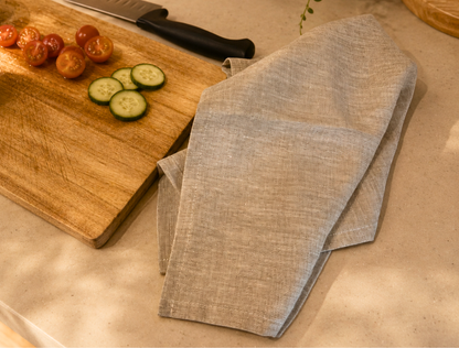 Gray towel on a kitchen counter with a cutting board and vegetables in the background