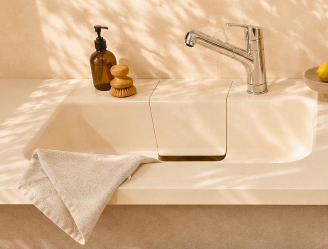 Beige sink with soap dispenser, brush, and towel on a neutral background